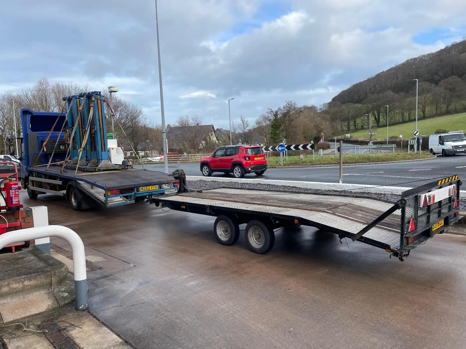 Twin-axle vehicle transport trailer beside a recovery truck